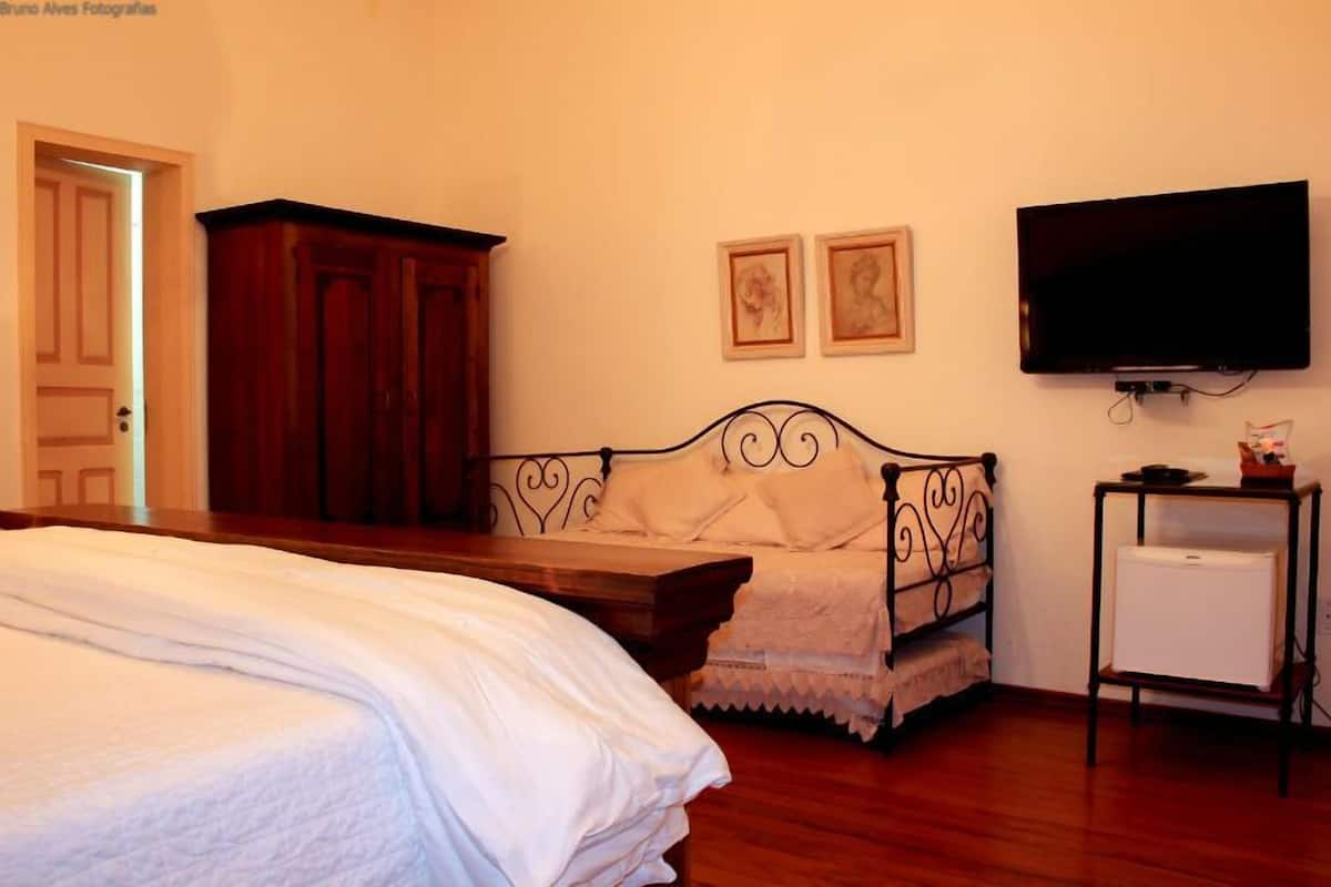 A bedroom with a bed, a wooden wardrobe, a television, and a small white cabinet.