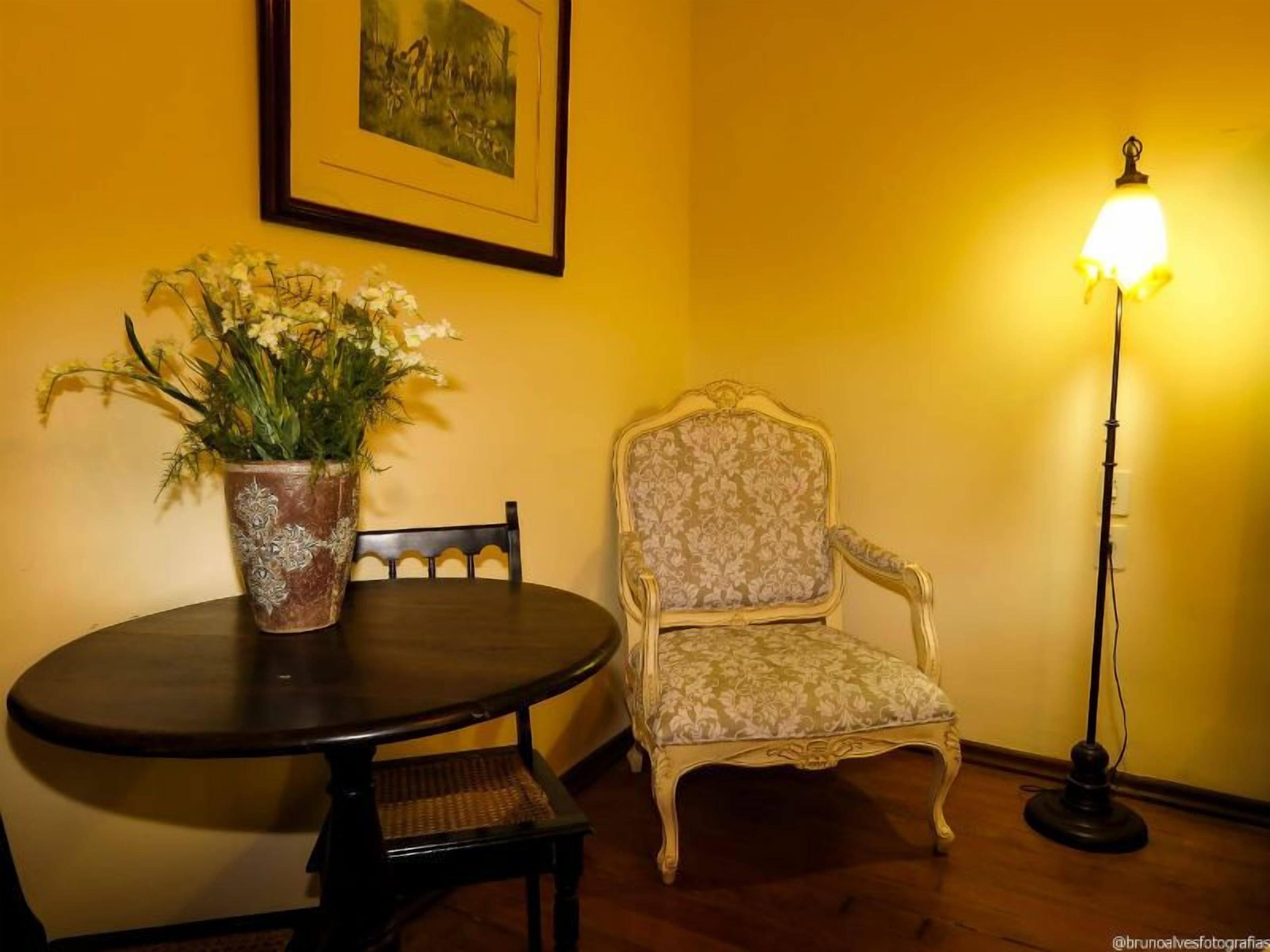 Una zona pranzo con un tavolo rotondo, una sedia, una pianta in vaso, un quadro appeso al muro e una lampada da terra.