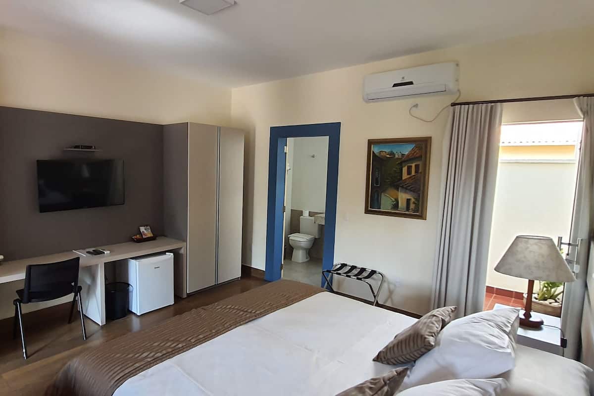 A hotel room with a bed, a desk with a chair, a television, a bathroom with a mirror, and a window with curtains.