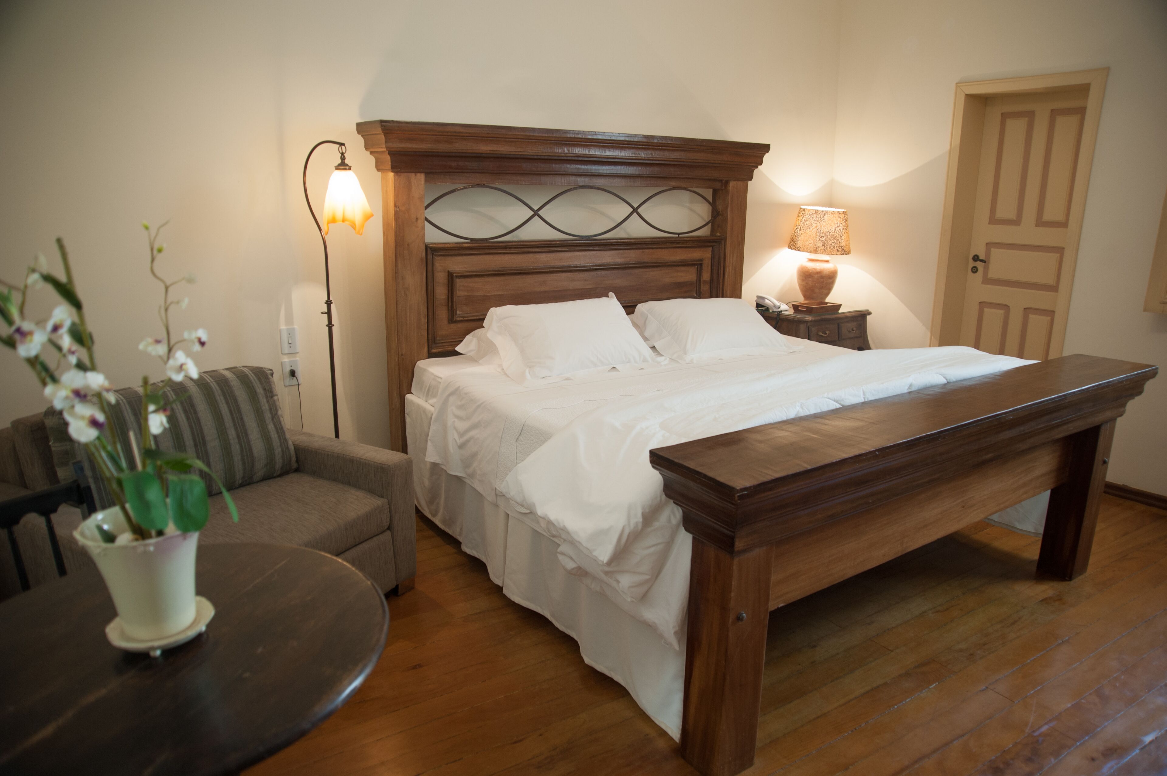 A neatly arranged bedroom with a wooden bed, bedside lamps, a wooden bench, a small table with a potted plant, and a sofa.