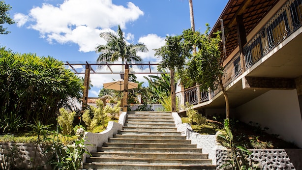 A staircase leading up to a building with a balcony, surrounded by greenery and a clear sky.