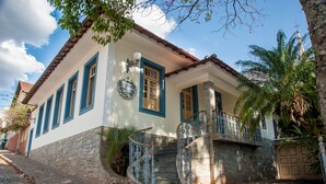 A two-story house with a stone facade, blue trim, and a staircase with ornate metal railings.