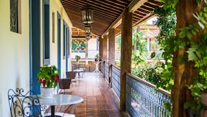 A covered outdoor patio with wooden flooring, metal railings, and potted plants.