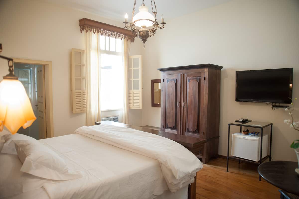A bedroom with a bed, a dresser, a television, and a small table with a plant.