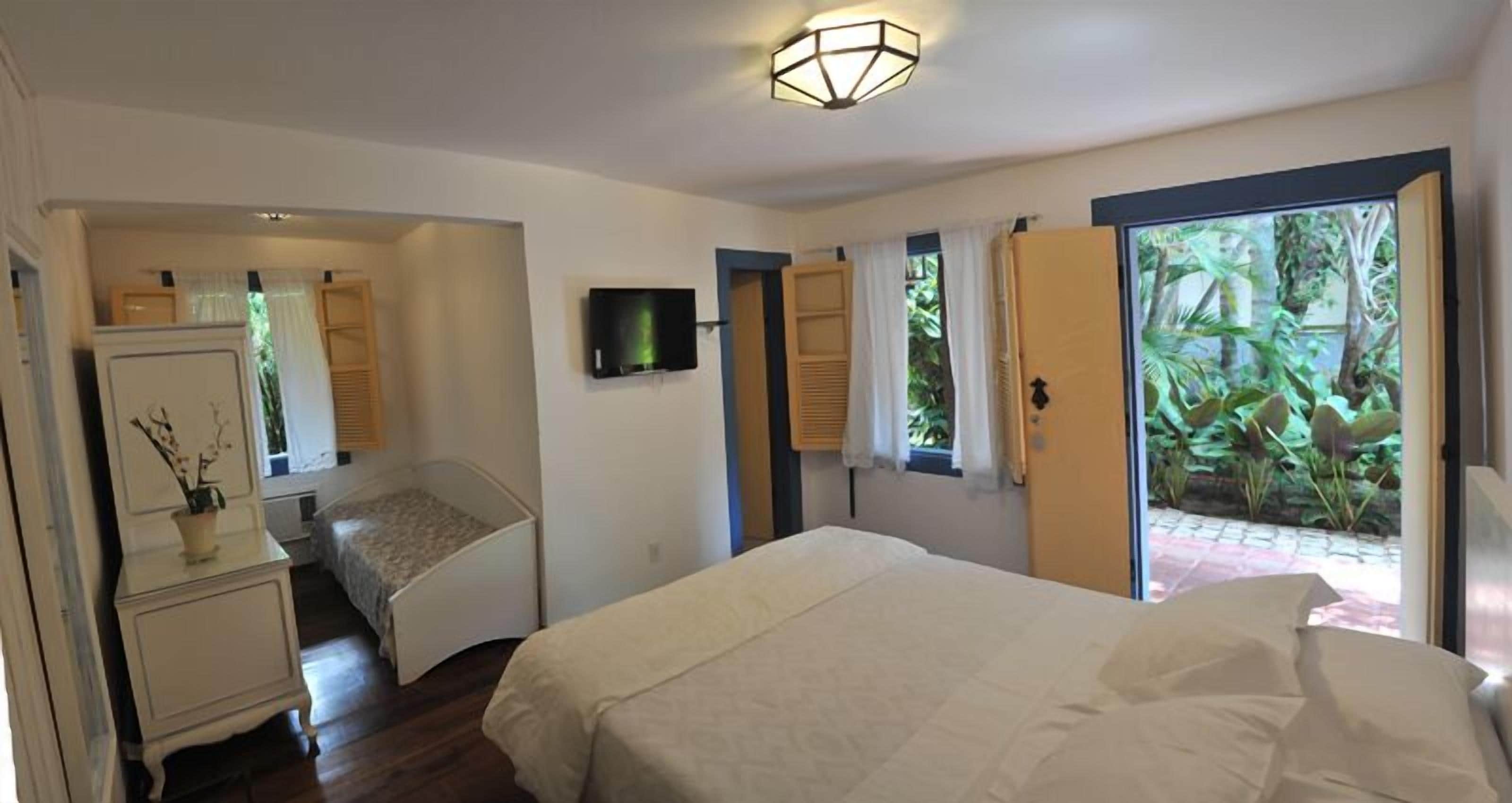 A bedroom with a bed, a television, a desk with a lamp, and a view of greenery outside.