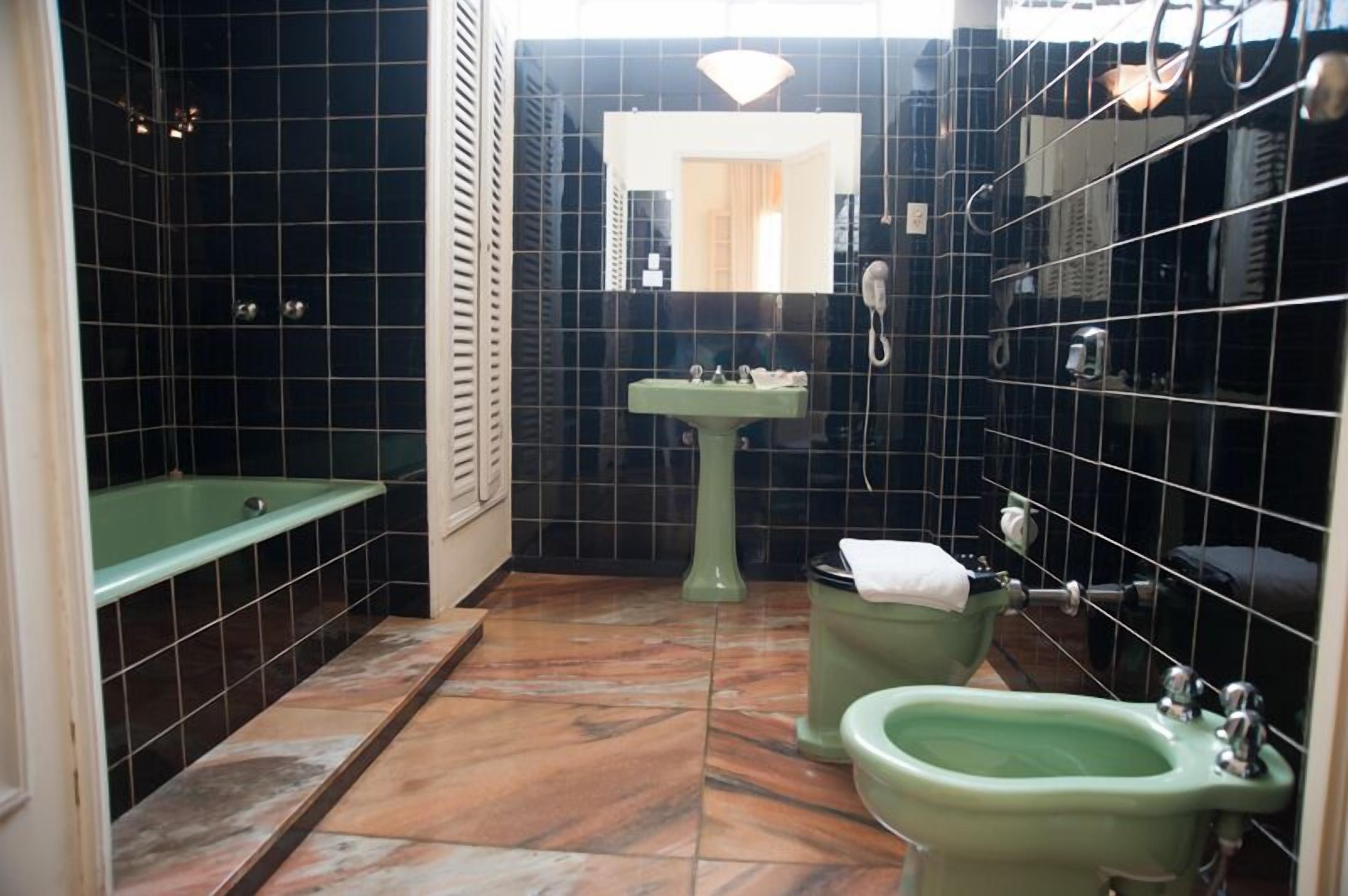 A bathroom with a green bathtub, a pedestal sink, and a bidet.