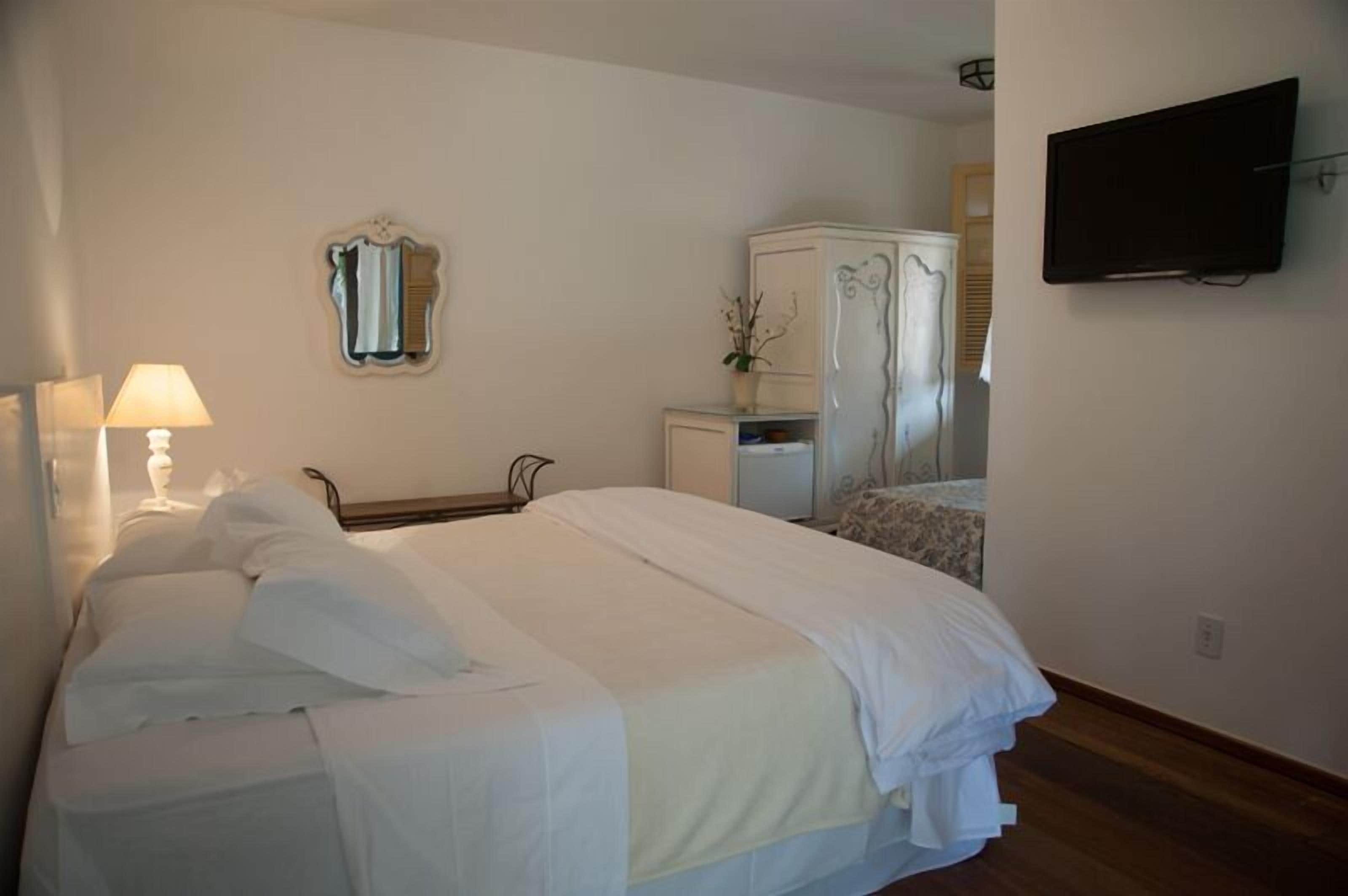 Une chambre d’hôtel avec un lit, une lampe de chevet, une commode, un miroir et un téléviseur.