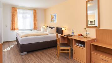 A hotel room with a bed, desk, chair, and a mirror.