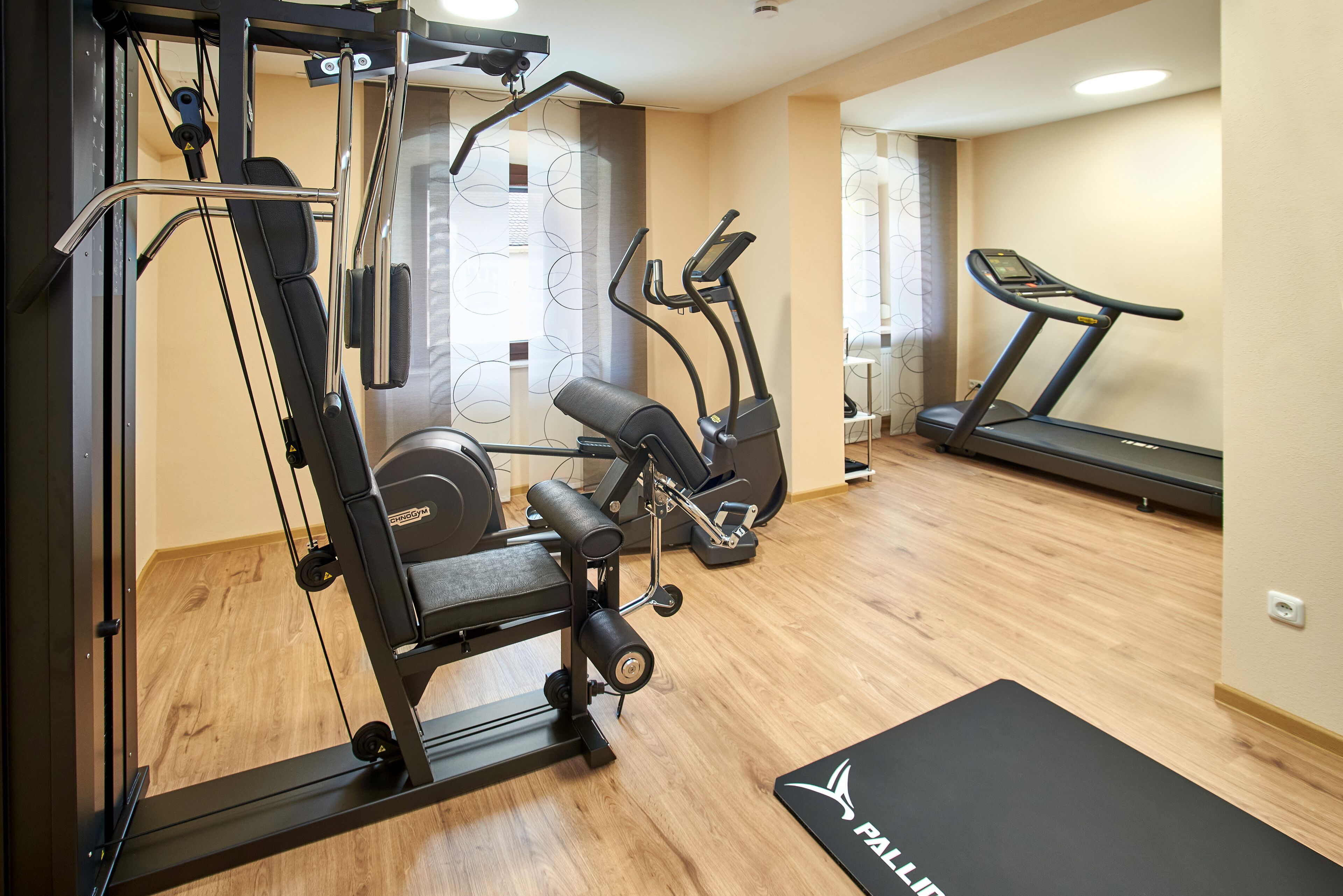 A gym with exercise equipment including a treadmill, elliptical, and weight machines.