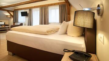 Habitación de hotel con una cama grande, teléfono en la mesita de noche, lámpara, televisor montado en la pared y escritorio con silla.