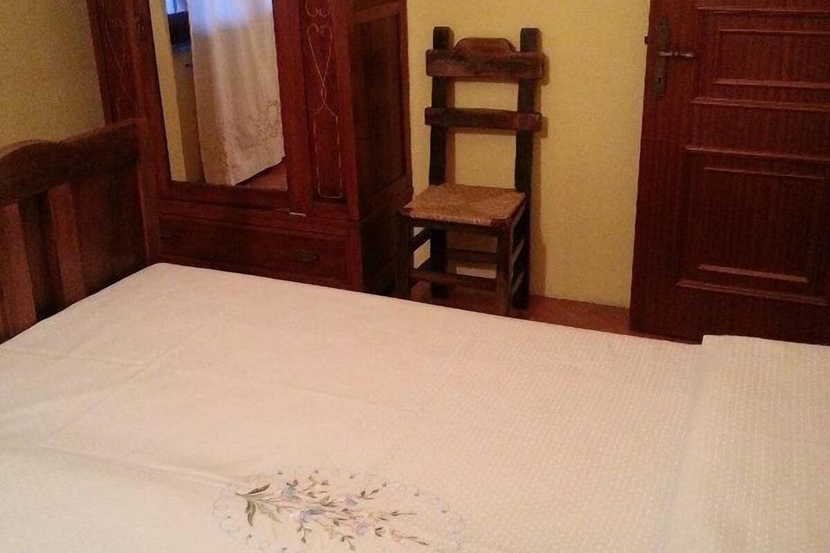 A room with a bed, a wooden wardrobe, a small wooden chair, and a door.