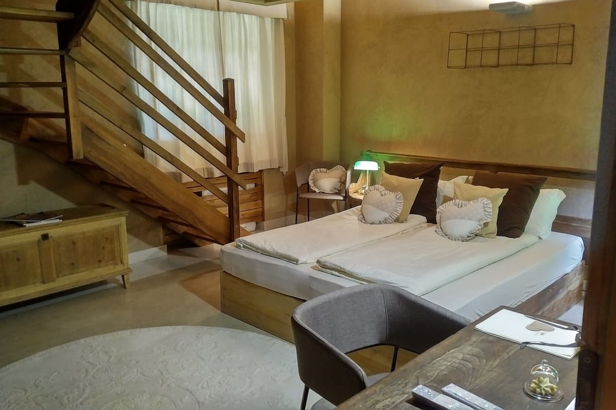 Un dormitorio con una escalera de madera, una cama con almohadas, una mesita de noche con una lámpara y una silla.