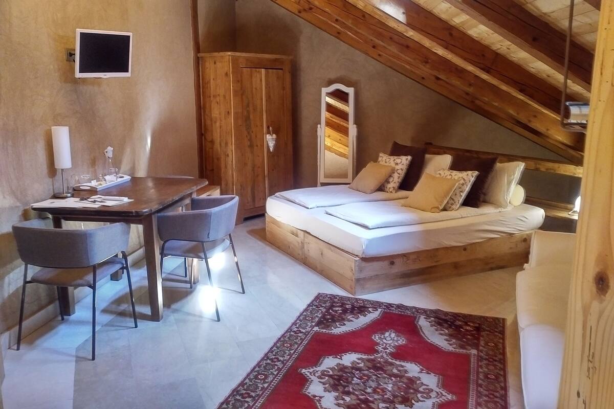 Un dormitorio acogedor en el ático, con techo de madera, una cama, un escritorio con sillas y un televisor.