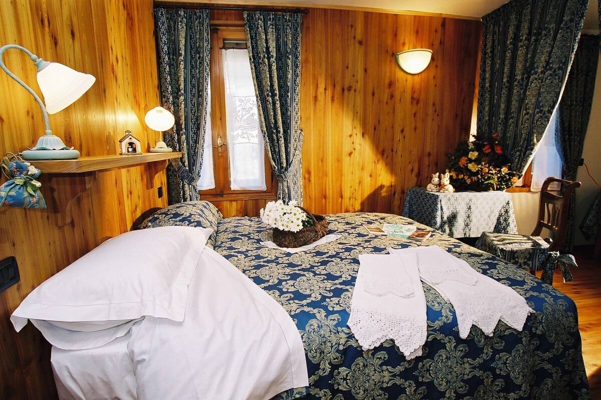 A wooden-paneled room with a bed, a nightstand, a lamp, and a window with curtains.