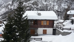 Een houten chalet met balkon, omgeven door besneeuwde bergen.