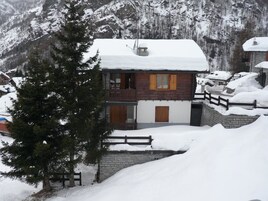Una cabaña de madera con balcón, rodeada de montañas nevadas.