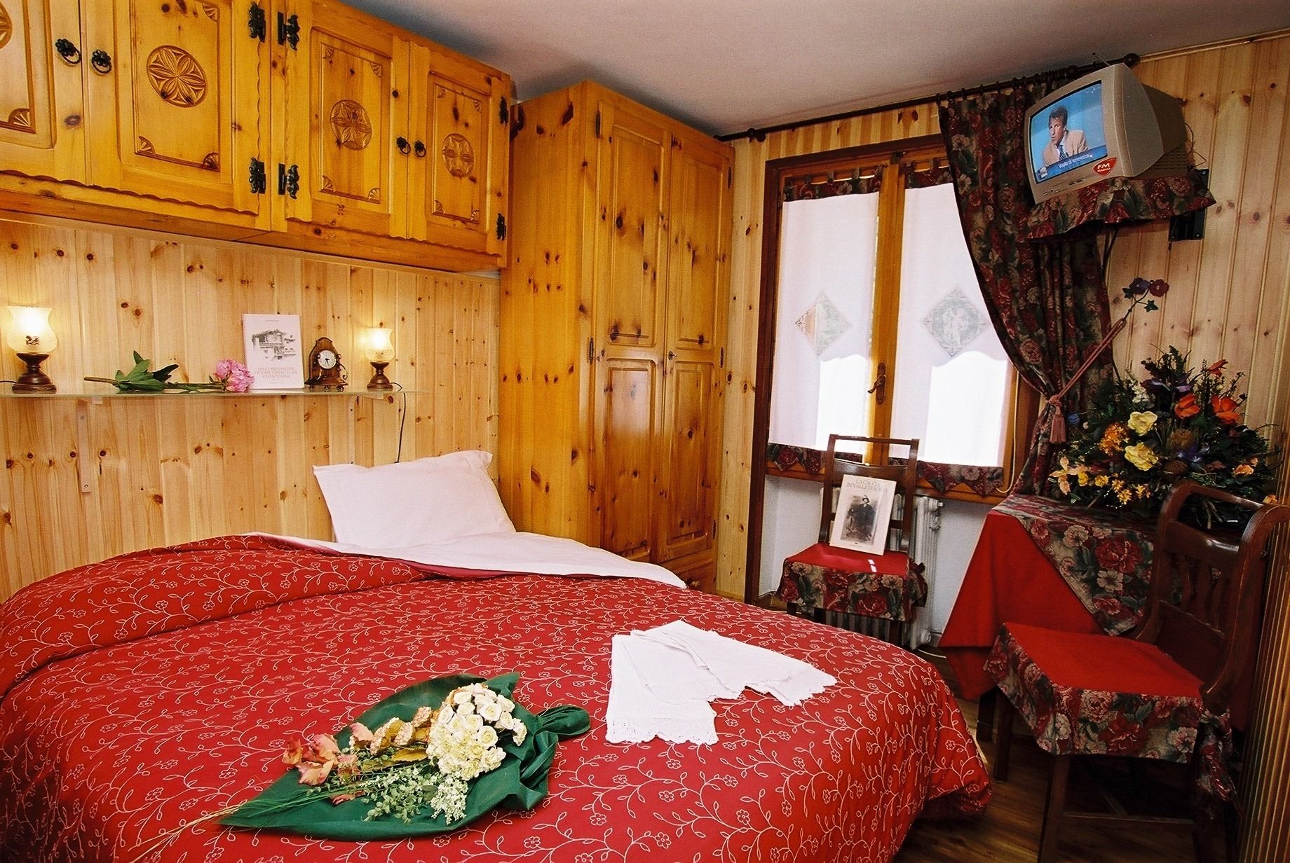 Ein Zimmer mit Holzboden, einem Bett, einem Fernseher und einer Blumenkomposition.