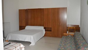 A bedroom with a bed, a wooden wardrobe, a small table, and a sofa. - Residence Cristallo (Alassio)