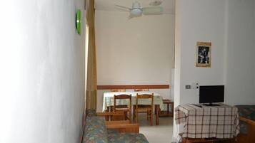 Una habitación con cama, una mesa con sillas, un televisor y un ventilador de techo.