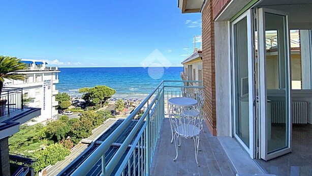 A balcony with a view of the sea, a table and chairs, and a building with a brick facade. - Residence Cristallo (Alassio)