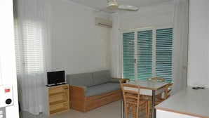 A compact living space with a sofa, a TV, a dining table with chairs, and a window with blinds. - Residence Cristallo (Alassio)