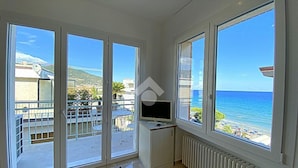 A room with large windows offering a view of the sea and a balcony with a table and chairs. - Residence Cristallo (Alassio)