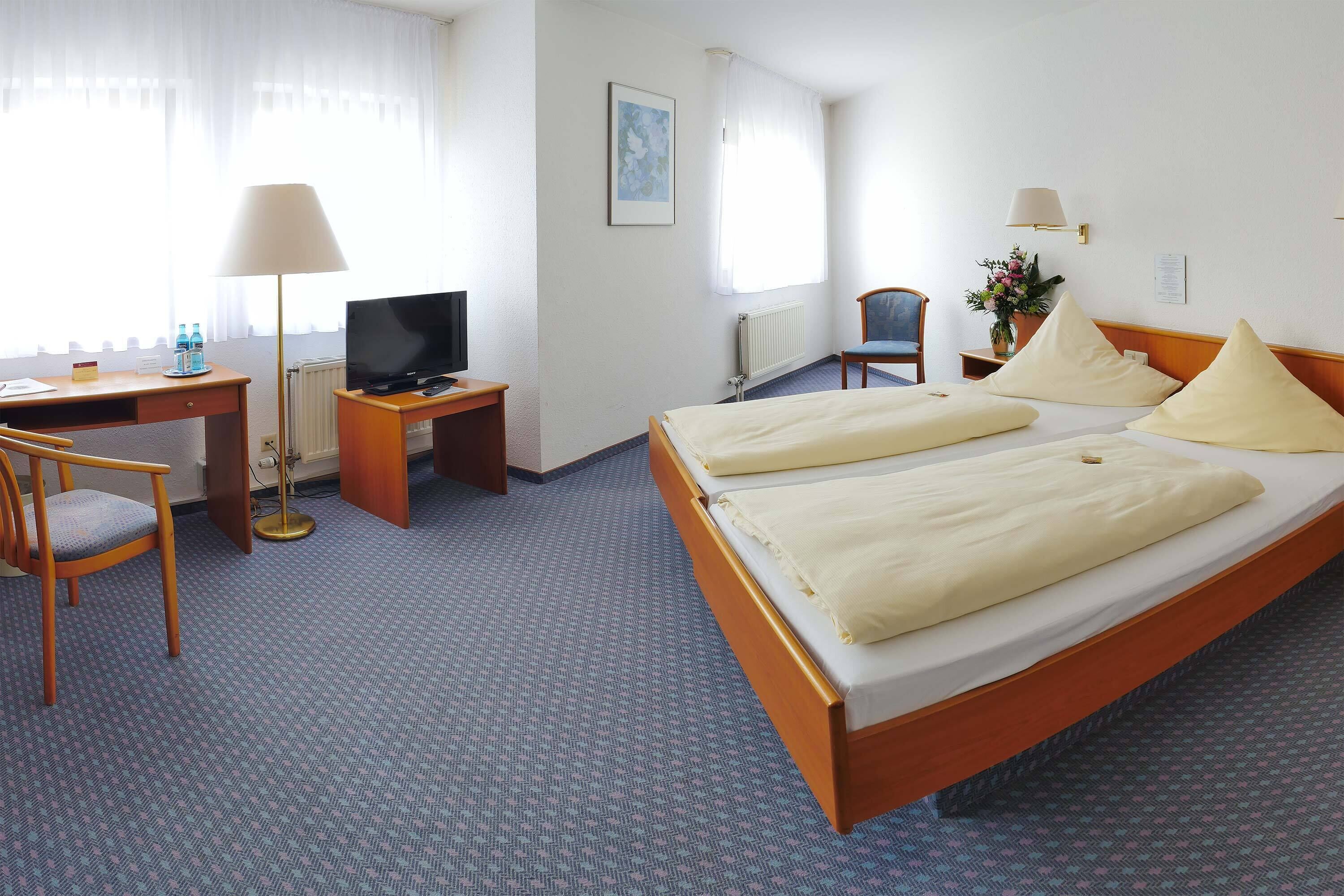 A hotel room with a bed, a desk, a chair, a TV, and a window with curtains.