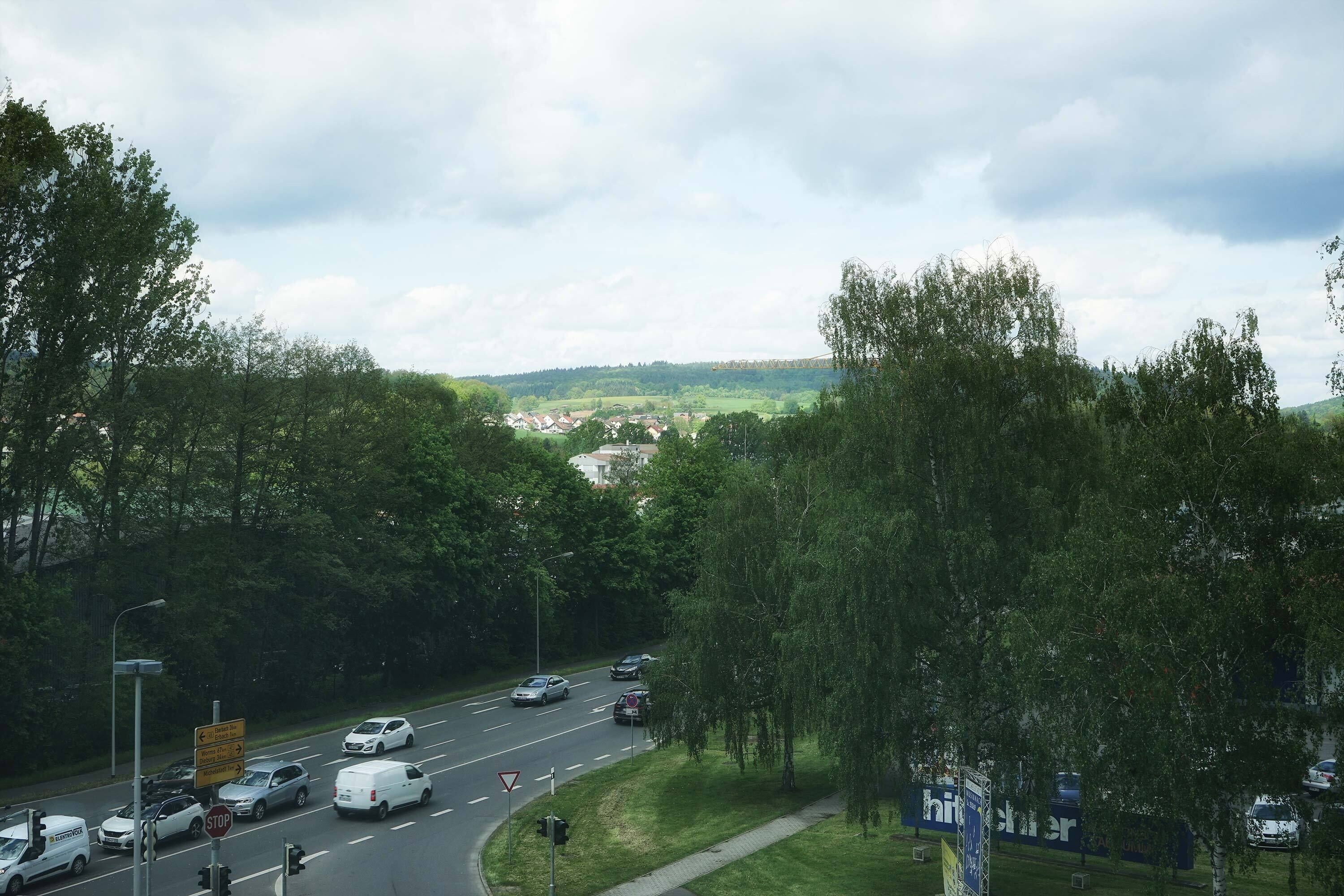 A road with multiple lanes and vehicles, surrounded by trees and greenery.