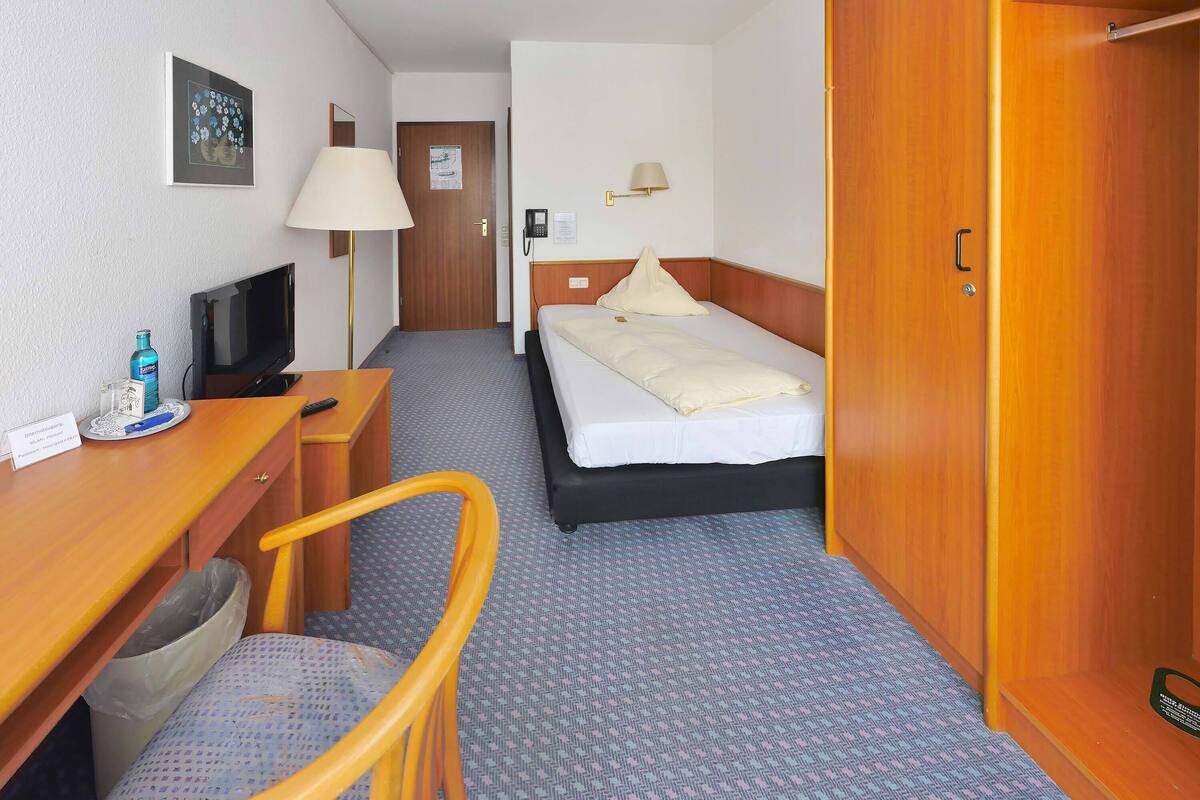 Ein Hotelzimmer mit Bett, Schreibtisch mit Computer, Stuhl, Lampe und Kleiderschrank.