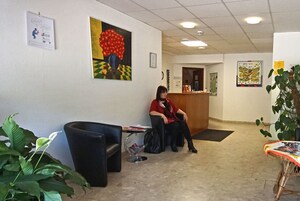 A reception area with a receptionist seated, a black sofa, a small table with magazines, and a potted plant.