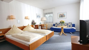 Hotelkamer met een tweepersoonsbed, een bureau met stoel, een bank, een televisie en een raam met gordijnen.
