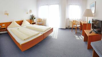 Et hotelværelse med dobbeltseng, skrivebord med stol, fjernsyn og et vindue med gardiner.