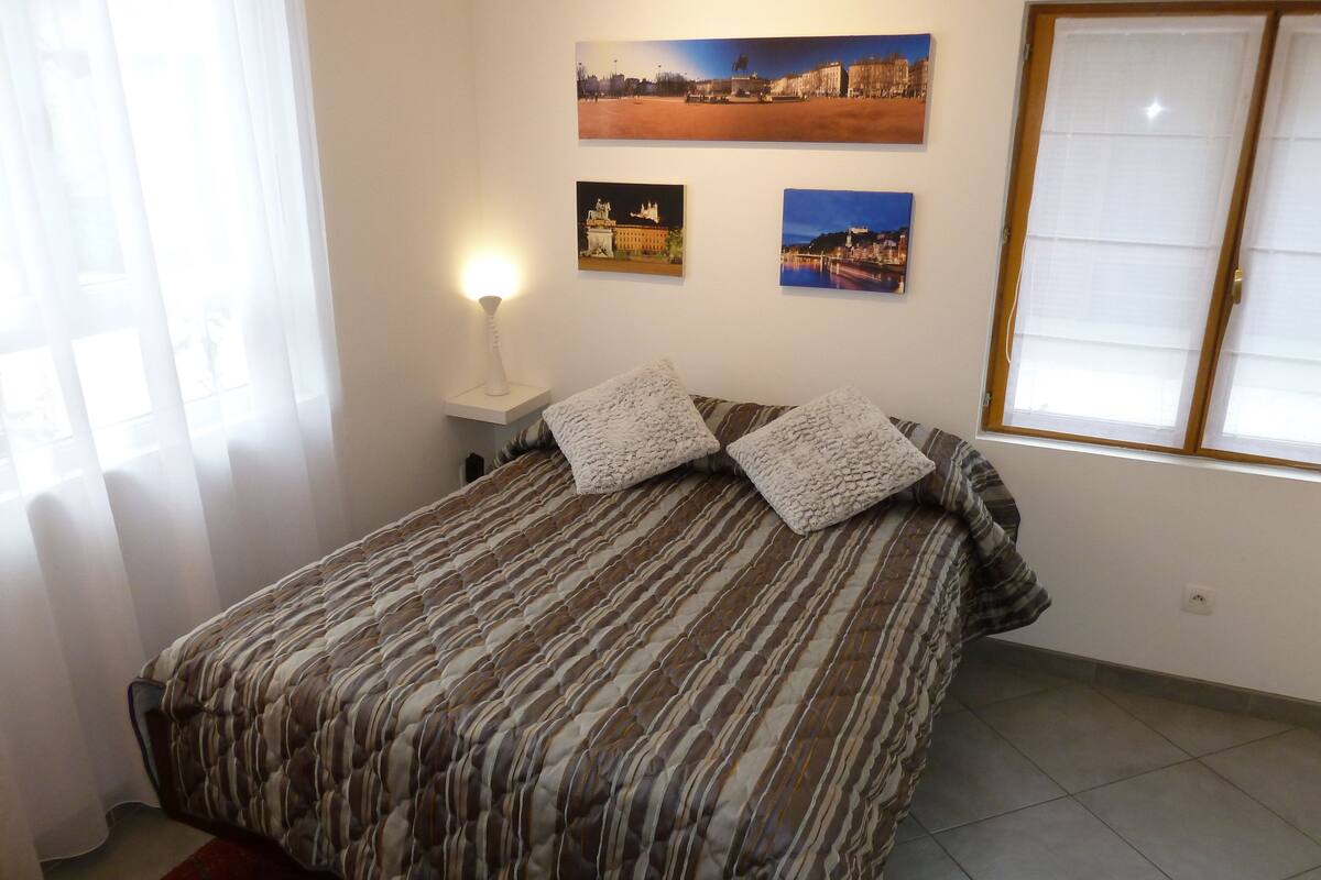 Quarto com colcha listrada, duas almofadas, mesa de cabeceira com abajur e três quadros na parede.