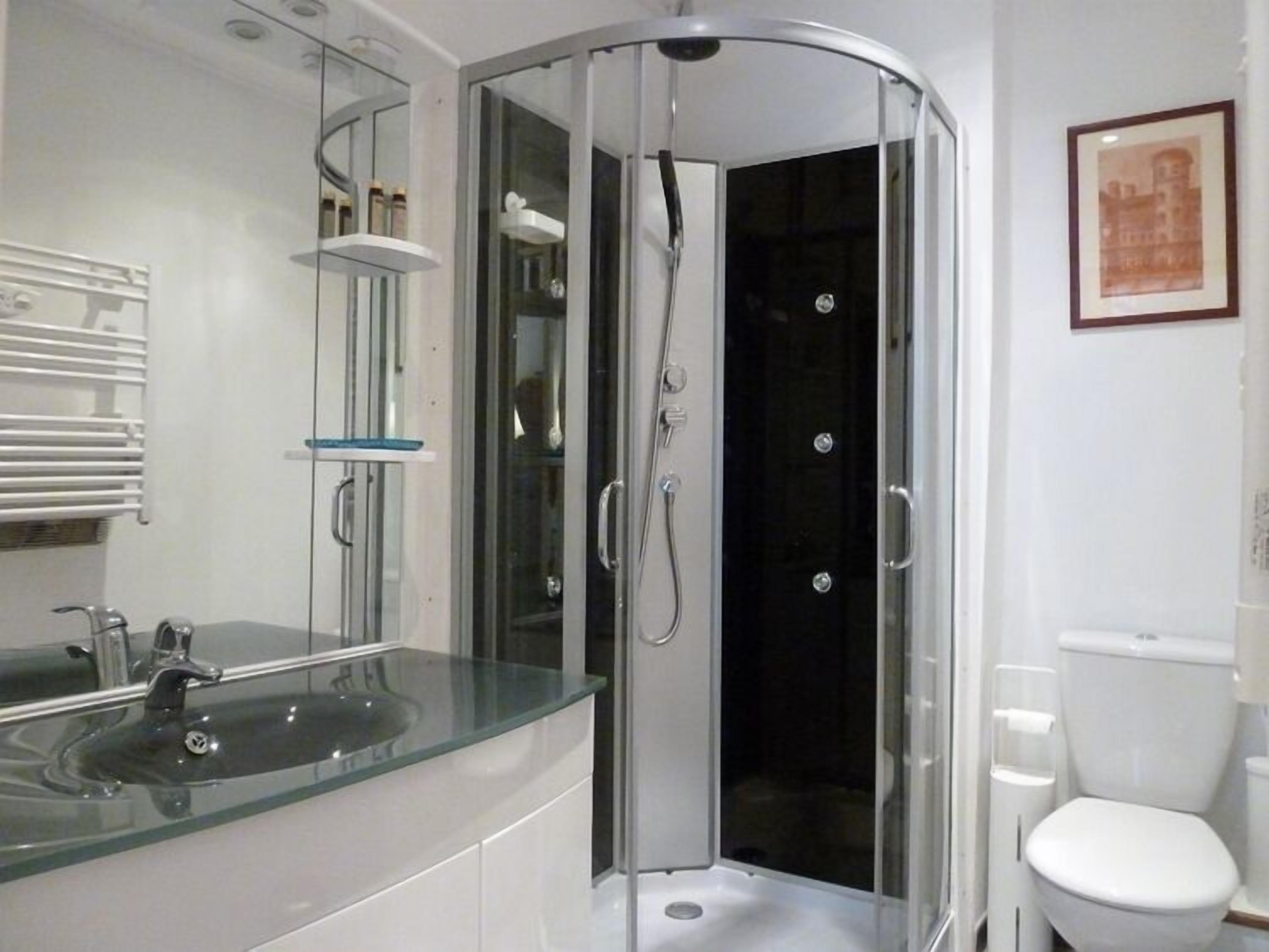 Un baño moderno con cabina de ducha de vidrio, un lavabo blanco y un inodoro.