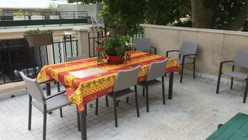 An outdoor patio with a table set for four, surrounded by chairs, and a potted plant on the table.