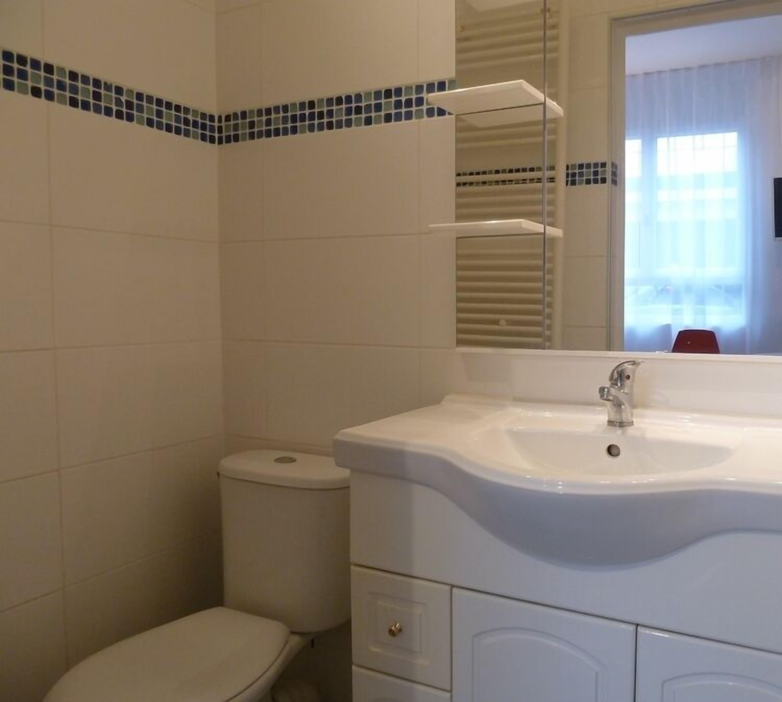 Un baño con lavamanos blanco, espejo y retrete.