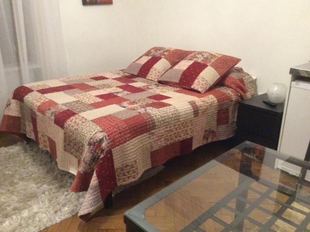 Una cama con colcha, una mesita de noche y una mesa con superficie de vidrio.