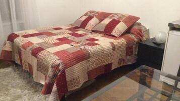 Una cama con colcha, una mesita de noche y una mesa con superficie de vidrio.