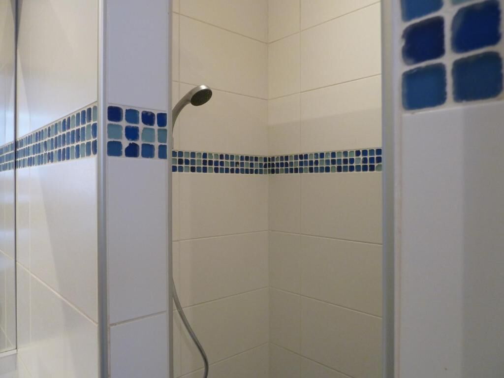 Un espace douche avec des carreaux blancs et une bordure en mosaïque bleue.