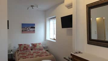 A bedroom with a bed, a bedside table, a TV, a window, and a mirror.