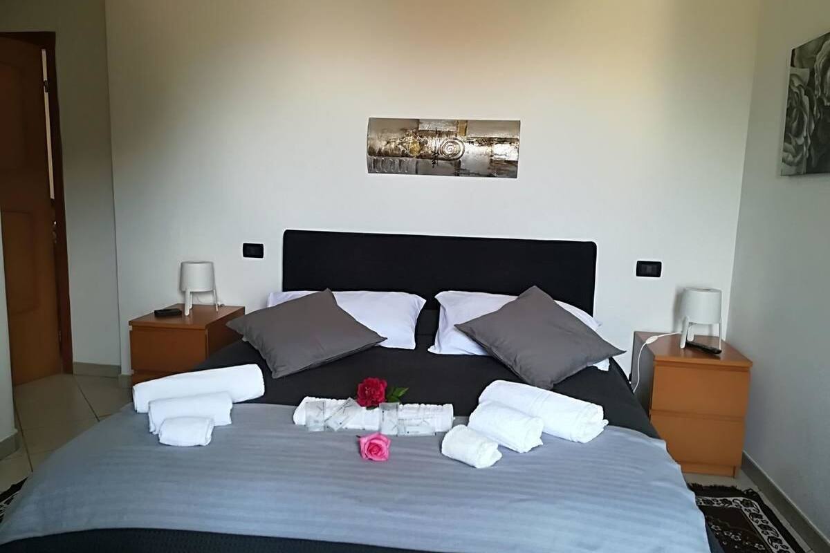 A neatly made bed with pillows, a folded towel, and a rose. There are two bedside tables with lamps.