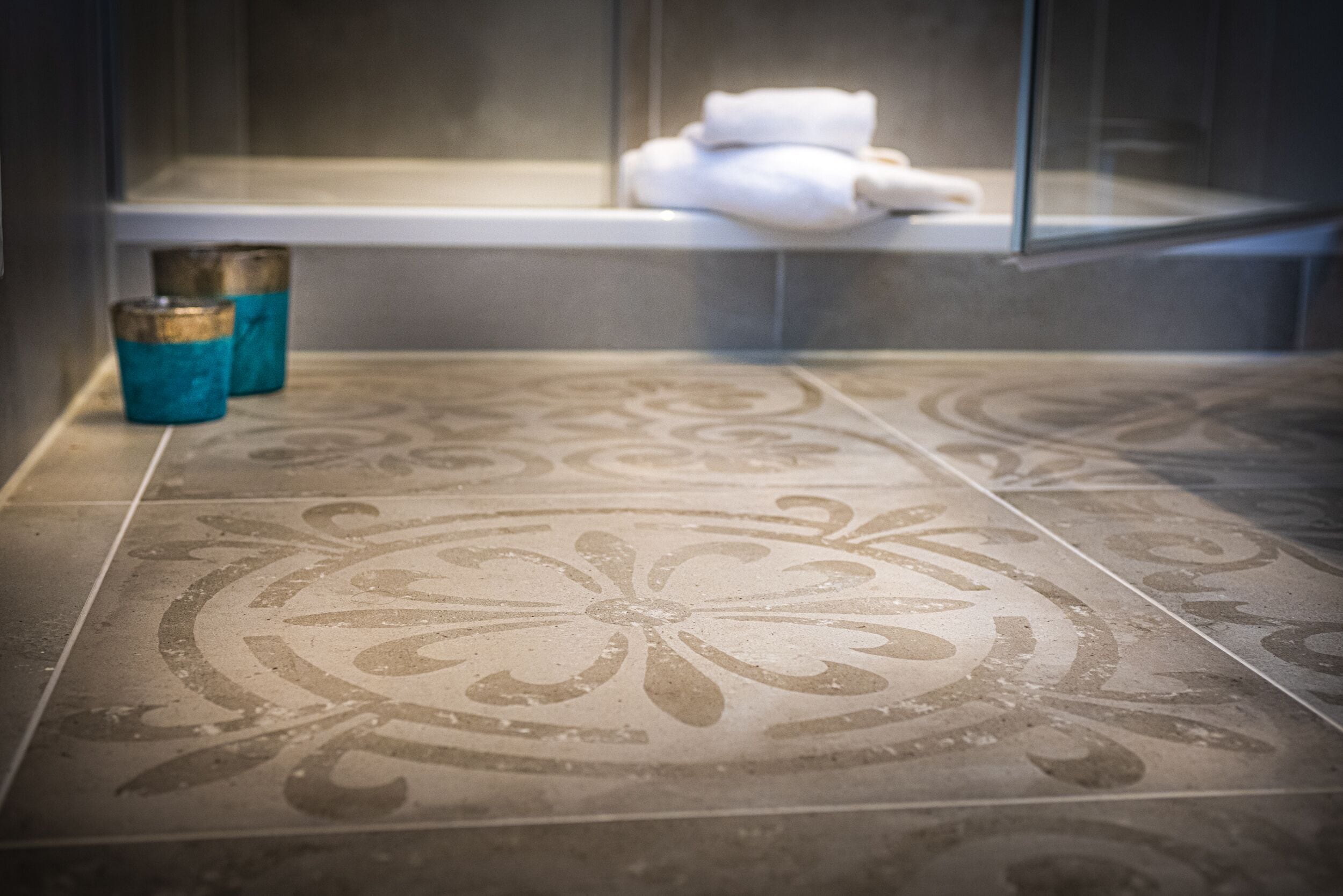 A bathroom with patterned tiles, a glass shower enclosure, and a towel rack with folded towels.