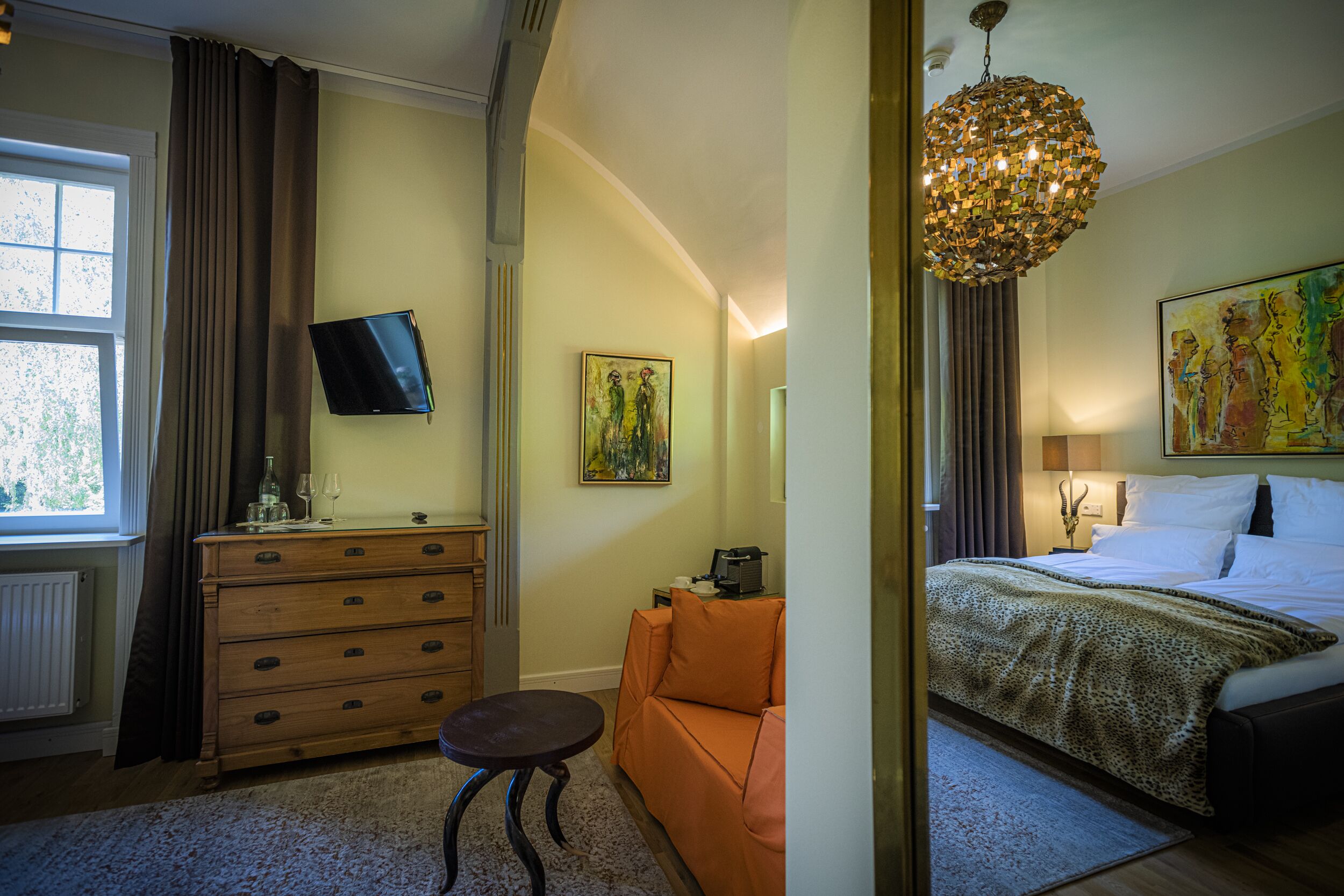 A hotel room with a bed, a desk, a chair, a dresser, a television, and artwork on the walls.