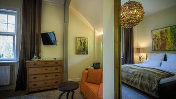 A hotel room with a bed, a desk, a chair, a dresser, a television, and artwork on the walls.