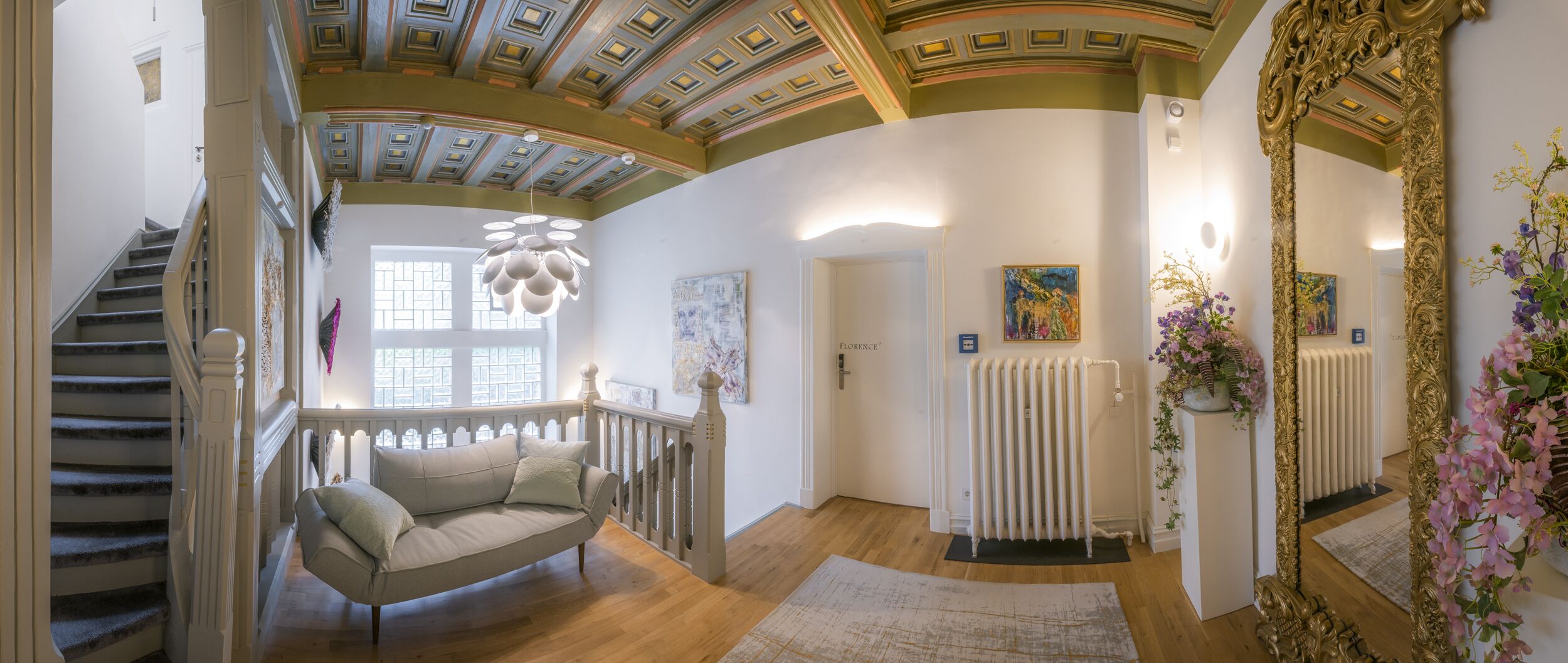 A spacious hallway with a curved ceiling, a staircase, a beige sofa, and a radiator.
