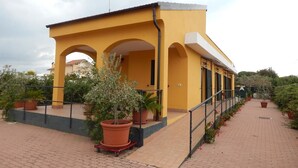 Un bâtiment jaune doté d’un patio couvert, de plantes en pot et d’une rambarde en métal.
