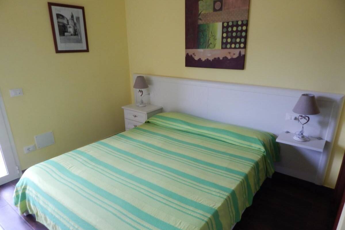 A bedroom with a bed, a nightstand, a lamp, and a wall with a framed picture and a colorful painting.