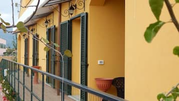 Un edificio amarillo con contraventanas verdes, barandilla metálica y plantas en macetas.
