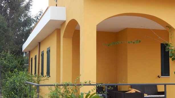 Un bâtiment jaune doté d’un patio couvert, de mobilier d’extérieur et d’une plante en pot.