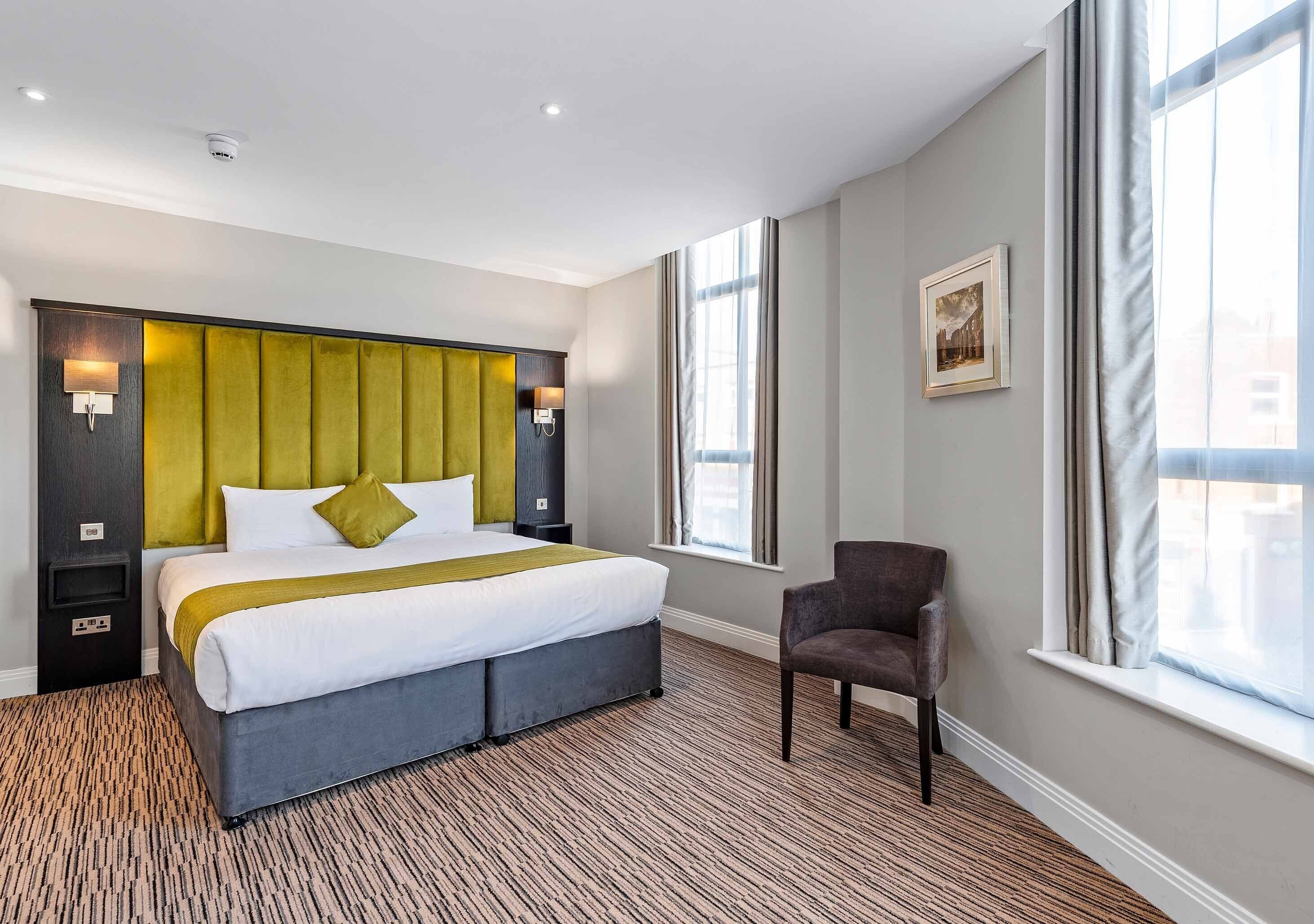 Une chambre d’hôtel avec un grand lit, deux tables de chevet, une chaise et une fenêtre avec des rideaux.